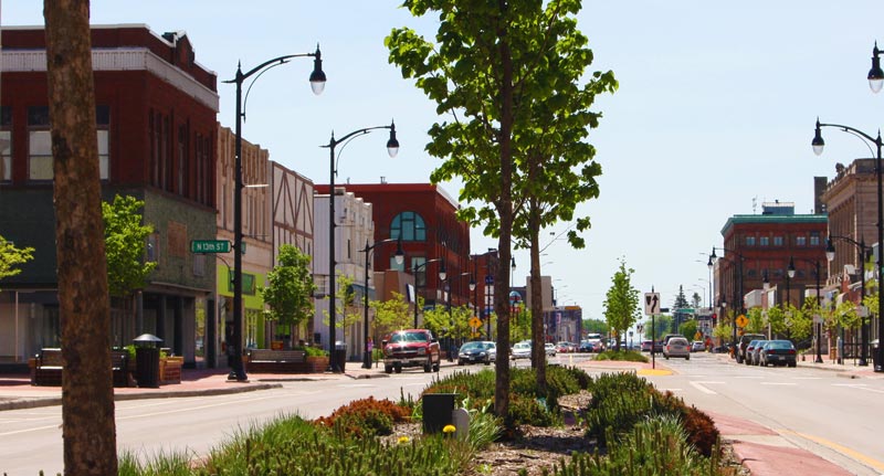 Street view of town with cars driving during a sunny day.