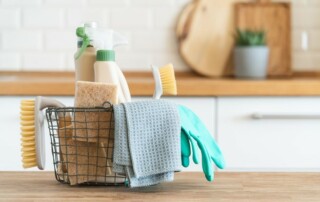 A basket of cleaning products and supplies sits on a wooden counter.